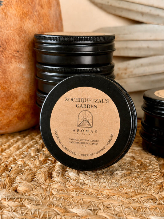 Aromas Aztecas discovery soy candle set with multiple fragrance and featuring Xochiquetzal's Garden samples in black aluminum tins on a woven textured surface with terracotta pottery and dried palm leaf décor.