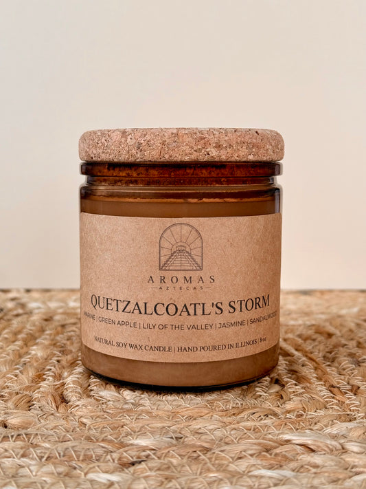 Aromas Aztecas Quetzalcoatl's Storm soy candle in an amber glass vessel with a cork lid on a woven textured surface.