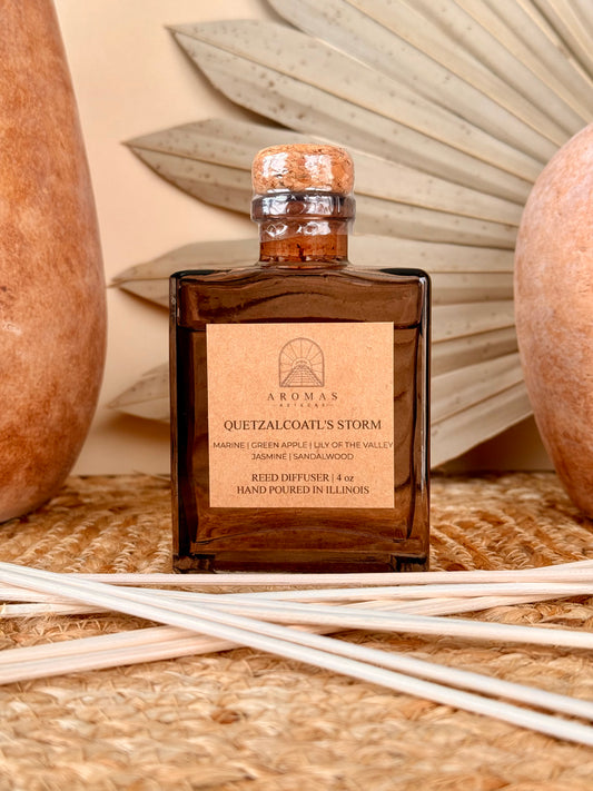 Aromas Aztecas Quetzalcoatl's Storm reed diffuser in an amber glass bottle with natural reeds on a woven textured surface with terracotta pottery and dried palm leaf décor.