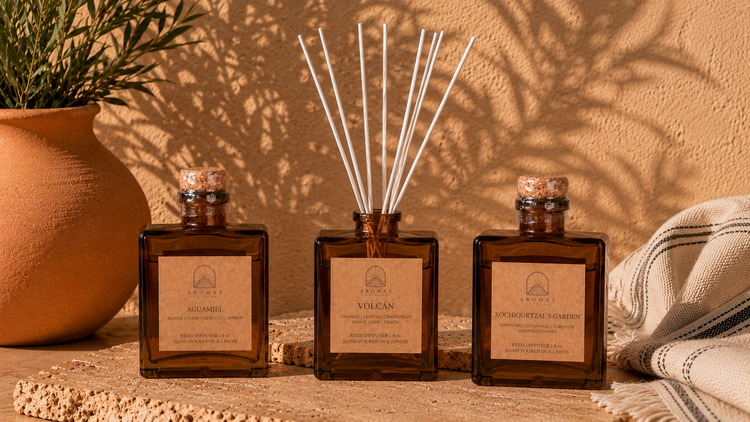 Three Aromas Aztecas reed diffusers featuring Quetzalcoatl's Storm, Volcán, and Xochiquetzal's Garden arranged with natural reeds, terracotta pottery, and warm earthy décor.