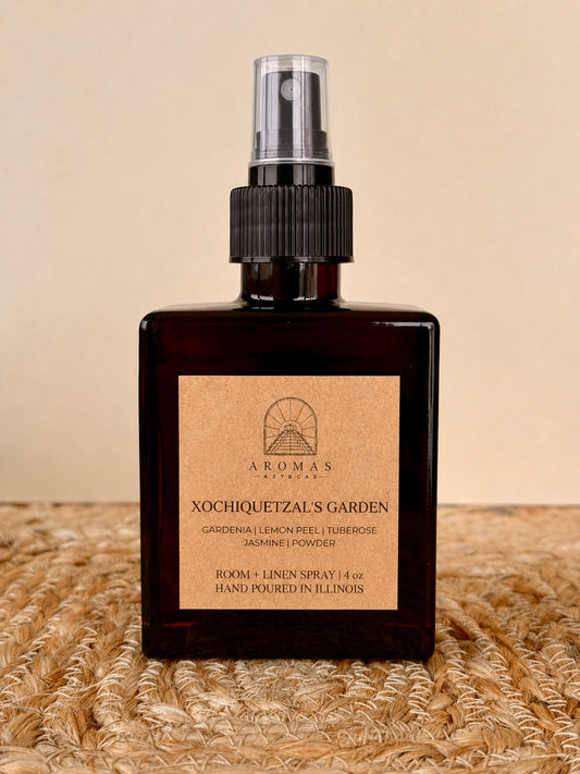 Aromas Aztecas Xochiquetzal's Garden room and linen spray in an amber glass bottle on a woven textured surface.