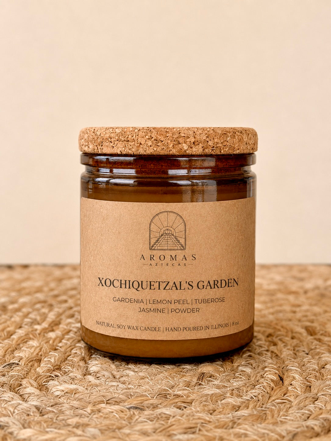 Aromas Aztecas Xochiquetzal's Garden soy candle in an amber glass vessel with a cork lid on a woven textured surface.