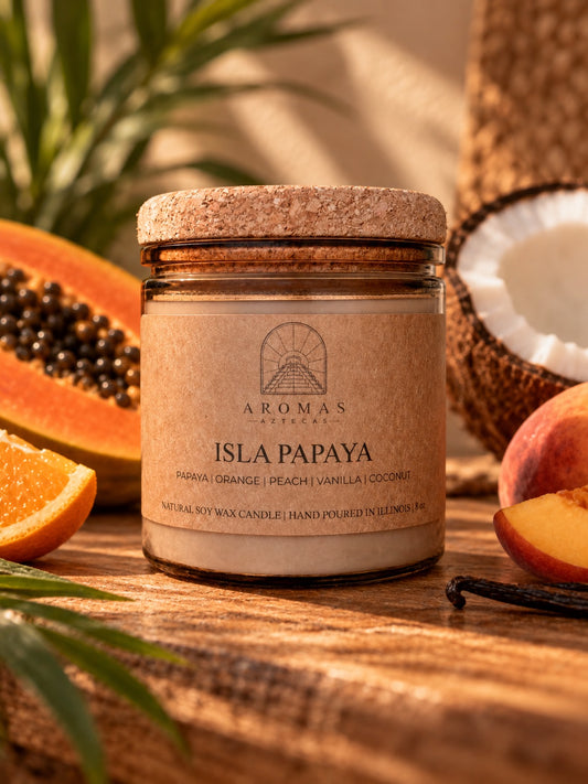 Aromas Aztecas Isla Papaya candle in an amber glass jar with a cork lid, displayed on a warm wooden surface with papaya, orange, peach, coconut, and vanilla surrounding it in soft golden light.