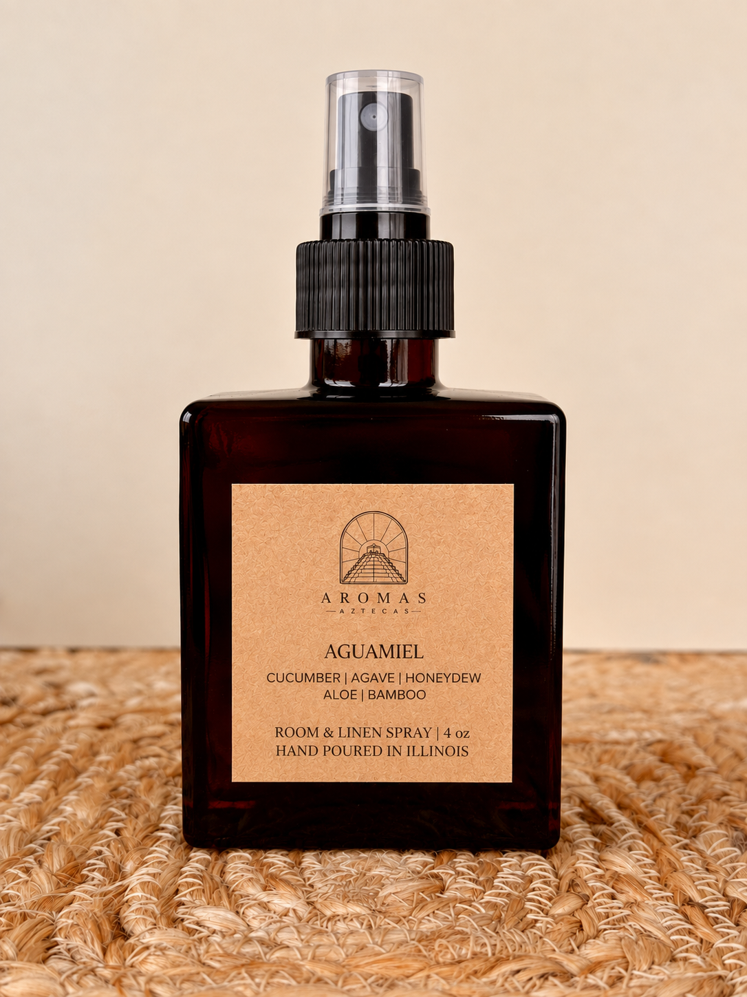 Aromas Aztecas Aguamiel room and linen spray in an amber glass bottle on a woven textured surface.