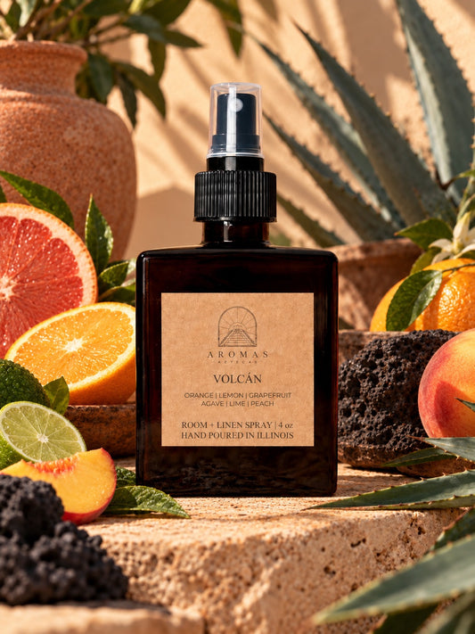 Aromas Aztecas Volcán room and linen spray surrounded by orange, lemon, grapefruit, lime, peach, agave, and volcanic stone in a sunlit setting.