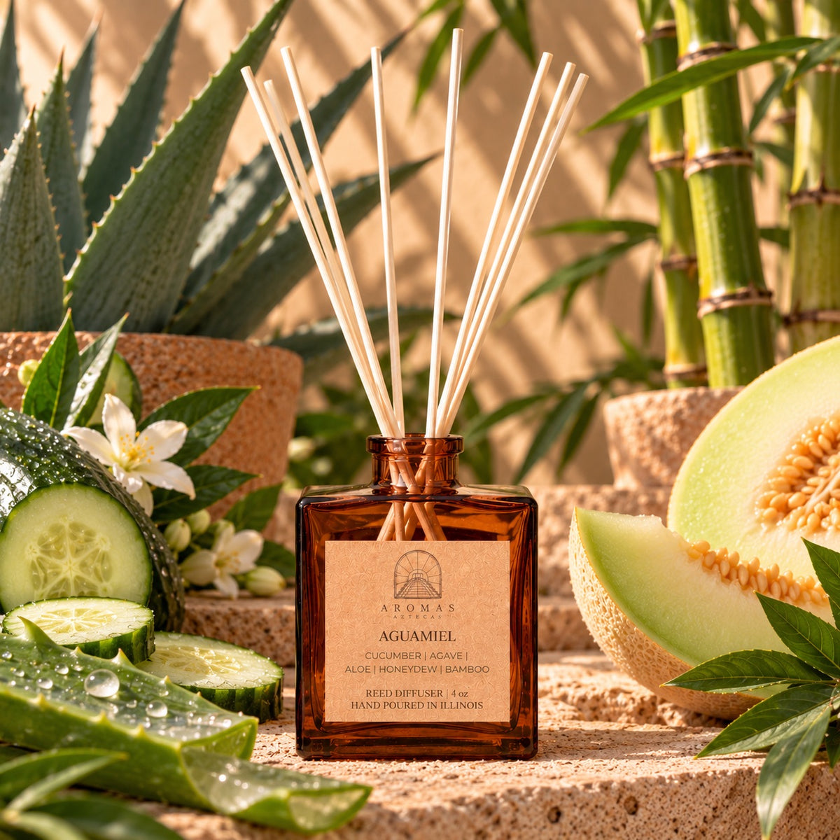 Aromas Aztecas Aguamiel reed diffuser in an amber glass bottle with natural reeds, surrounded by cucumber, aloe, honeydew, agave, bamboo, greenery, and warm stone accents against a sunlit background.