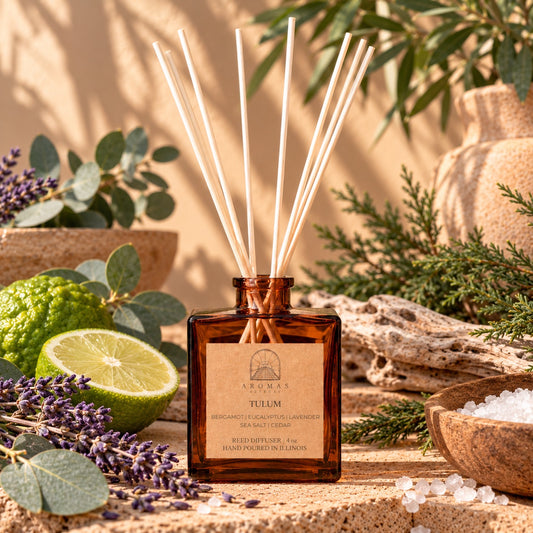 Aromas Aztecas Tulum reed diffuser in an amber glass bottle with natural reeds, surrounded by lime, lavender, eucalyptus, cedar, sea salt, driftwood, and botanical accents against a sunlit background.