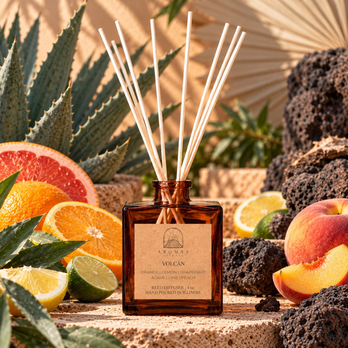 Aromas Aztecas Volcán reed diffuser in an amber glass bottle with natural reeds, surrounded by orange, lemon, grapefruit, lime, peach, agave, and volcanic stone in a sunlit setting.