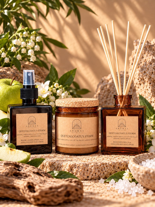 Aromas Aztecas Quetzalcoatl’s Storm fragrance collection featuring an amber glass room + linen spray, amber glass soy candle, and amber glass reed diffuser with natural reeds inserted, styled with green apple, marine-inspired elements, white florals, and natural stone accents against a sunlit background.