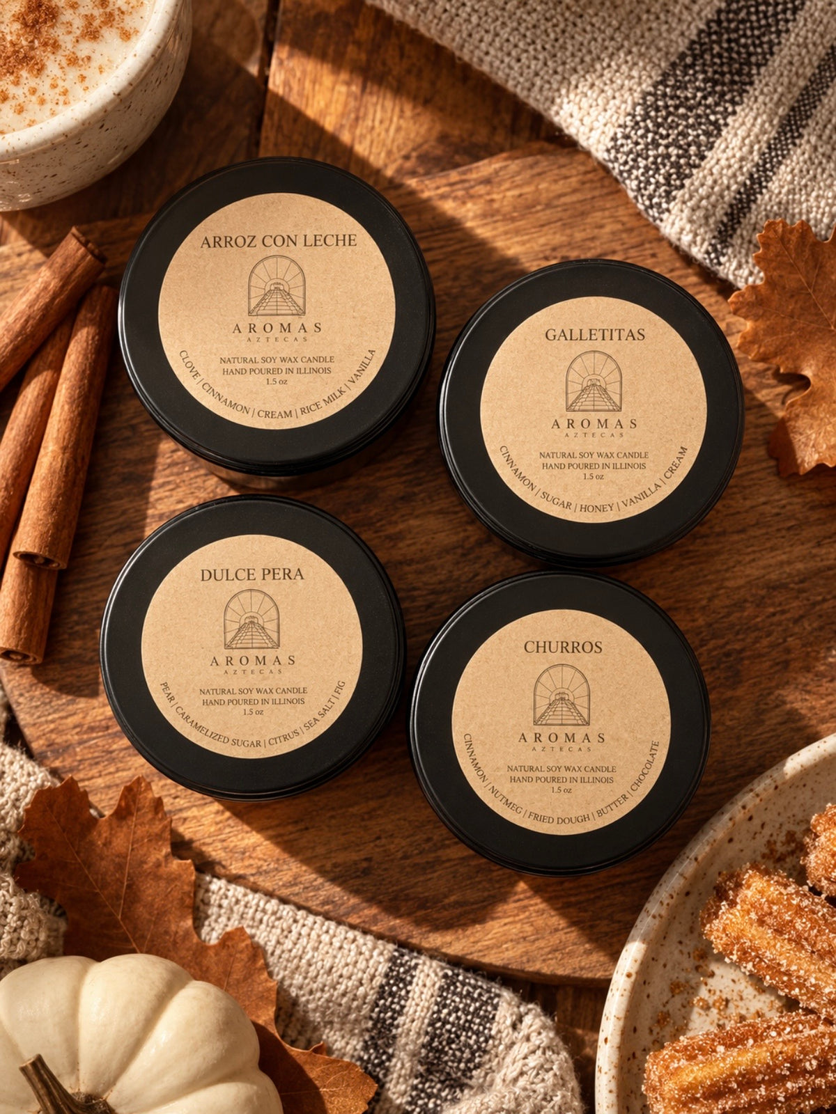 Top-down photo of four Aromas Aztecas 1.5 oz discovery candles arranged on a rustic wooden surface, featuring Arroz con Leche, Galletitas, Dulce Pera, and Churros. The candles are surrounded by fall leaves, terracotta fabric, a small pumpkin, and seasonal accents.