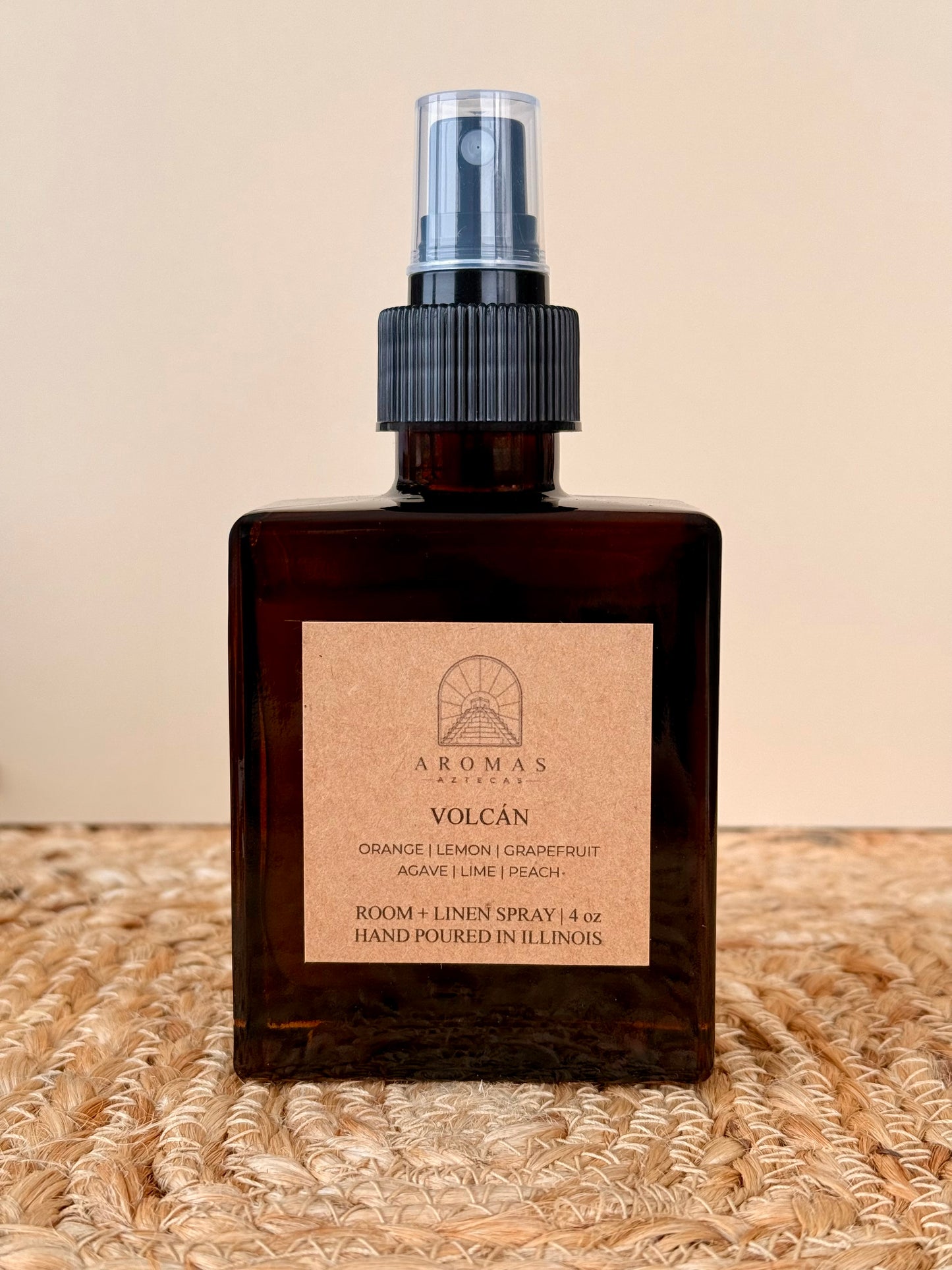 Aromas Aztecas Volcán room and linen spray in an amber glass bottle on a woven textured surface.