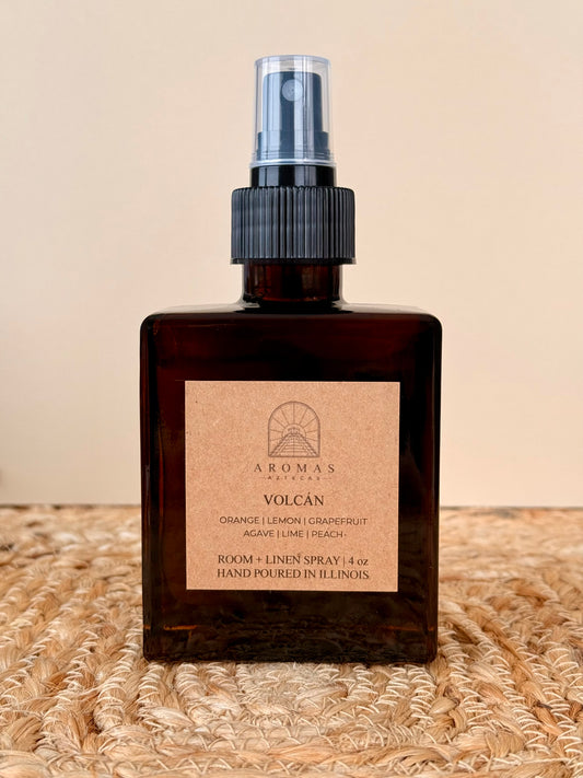 Aromas Aztecas Volcán room and linen spray in an amber glass bottle on a woven textured surface.