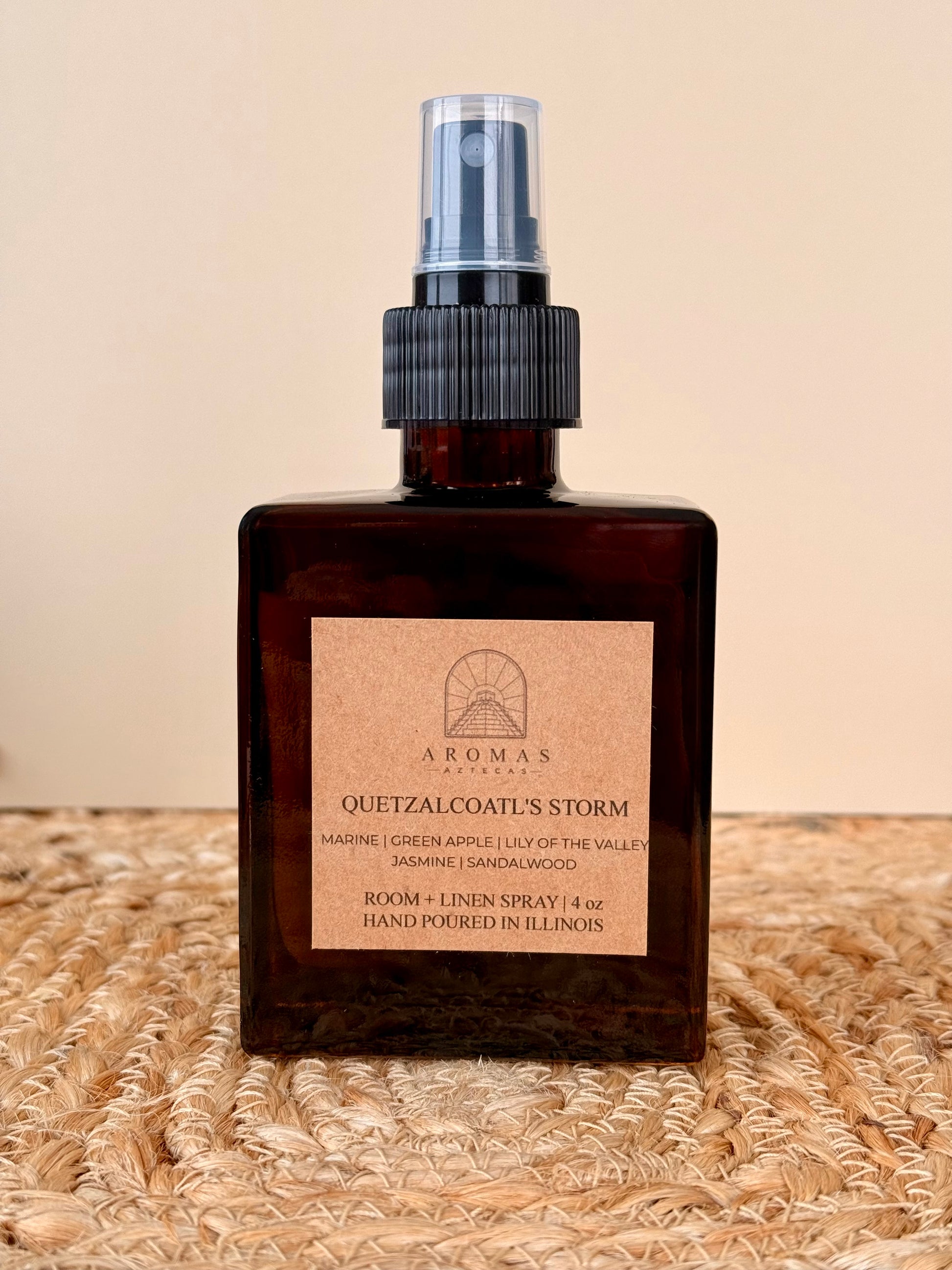 Aromas Aztecas Quetzalcoatl's Storm room and linen spray in an amber glass bottle on a woven textured surface.