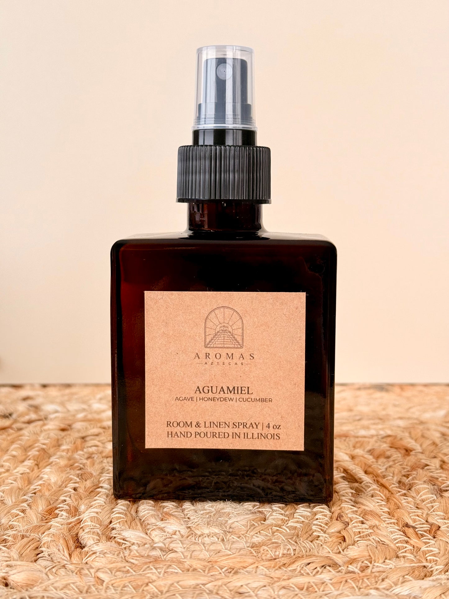 Aromas Aztecas Aguamiel room and linen spray in an amber glass bottle on a woven textured surface.