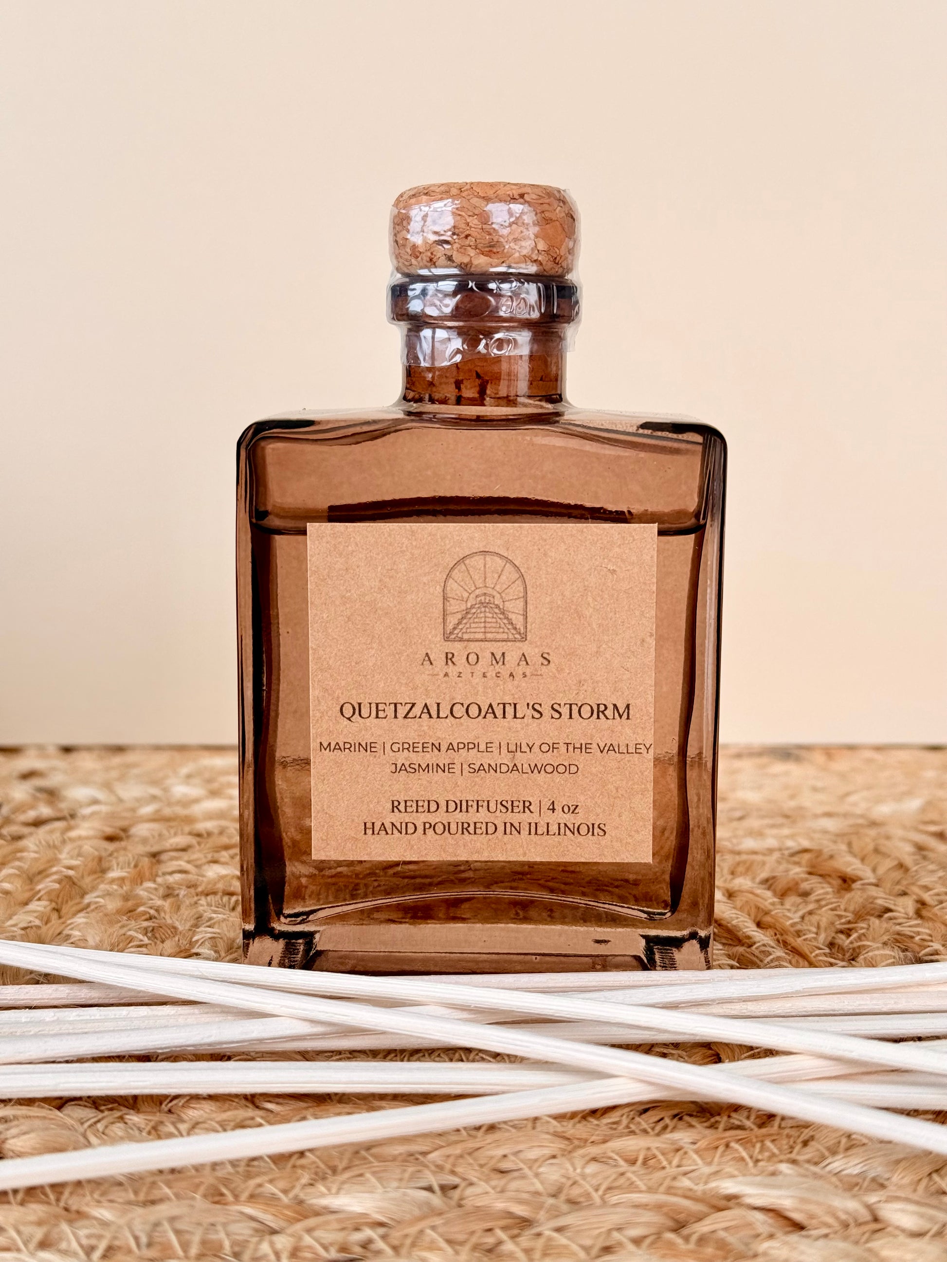 Aromas Aztecas Quetzalcoatl's Storm reed diffuser in an amber glass bottle with natural reeds on a woven textured surface.