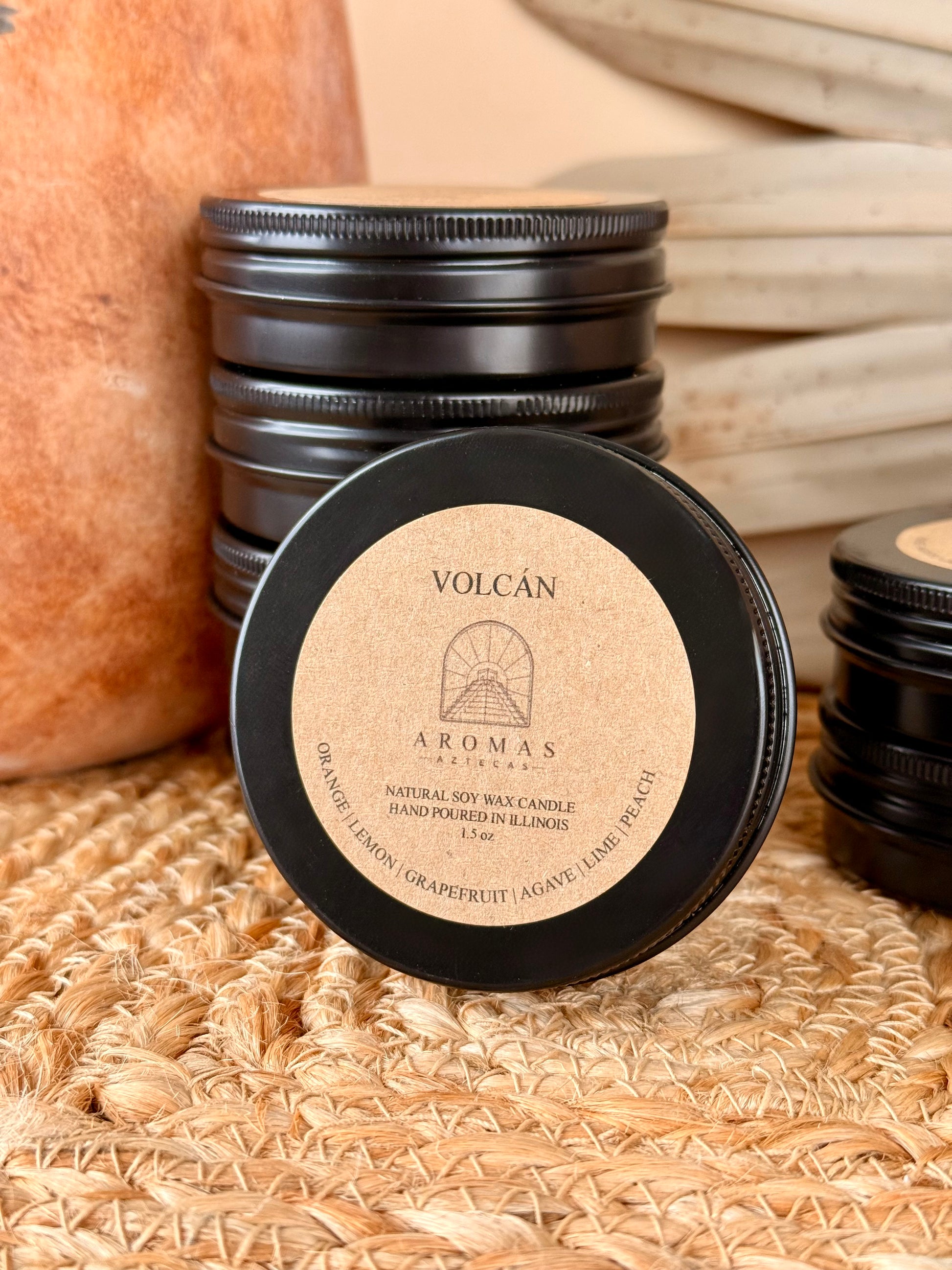 Aromas Aztecas discovery soy candle set with multiple fragrance samples and featuring Volcán in black aluminum tins on a woven textured surface with terracotta pottery and dried palm leaf décor.