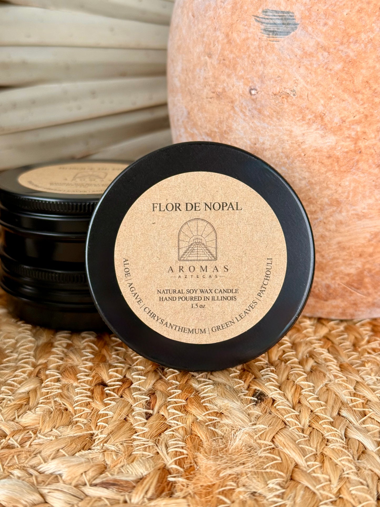 Aromas Aztecas discovery soy candle set with multiple fragrance samples featuring Flor de Nopal in black aluminum tins on a woven textured surface with terracotta pottery and dried palm leaf décor.