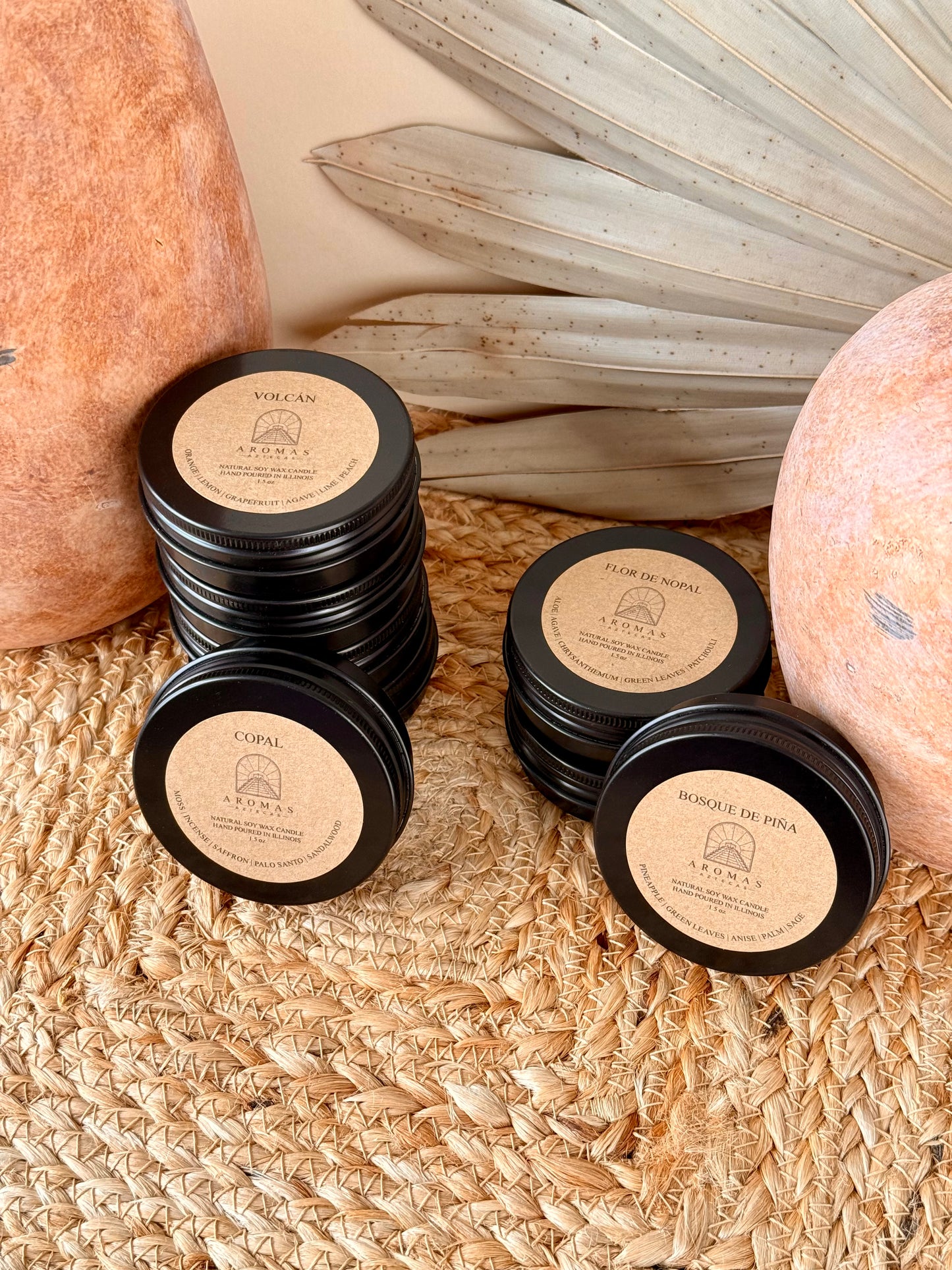 Aromas Aztecas discovery soy candle set with multiple fragrance samples in black aluminum tins on a woven textured surface with terracotta pottery and dried palm leaf décor.