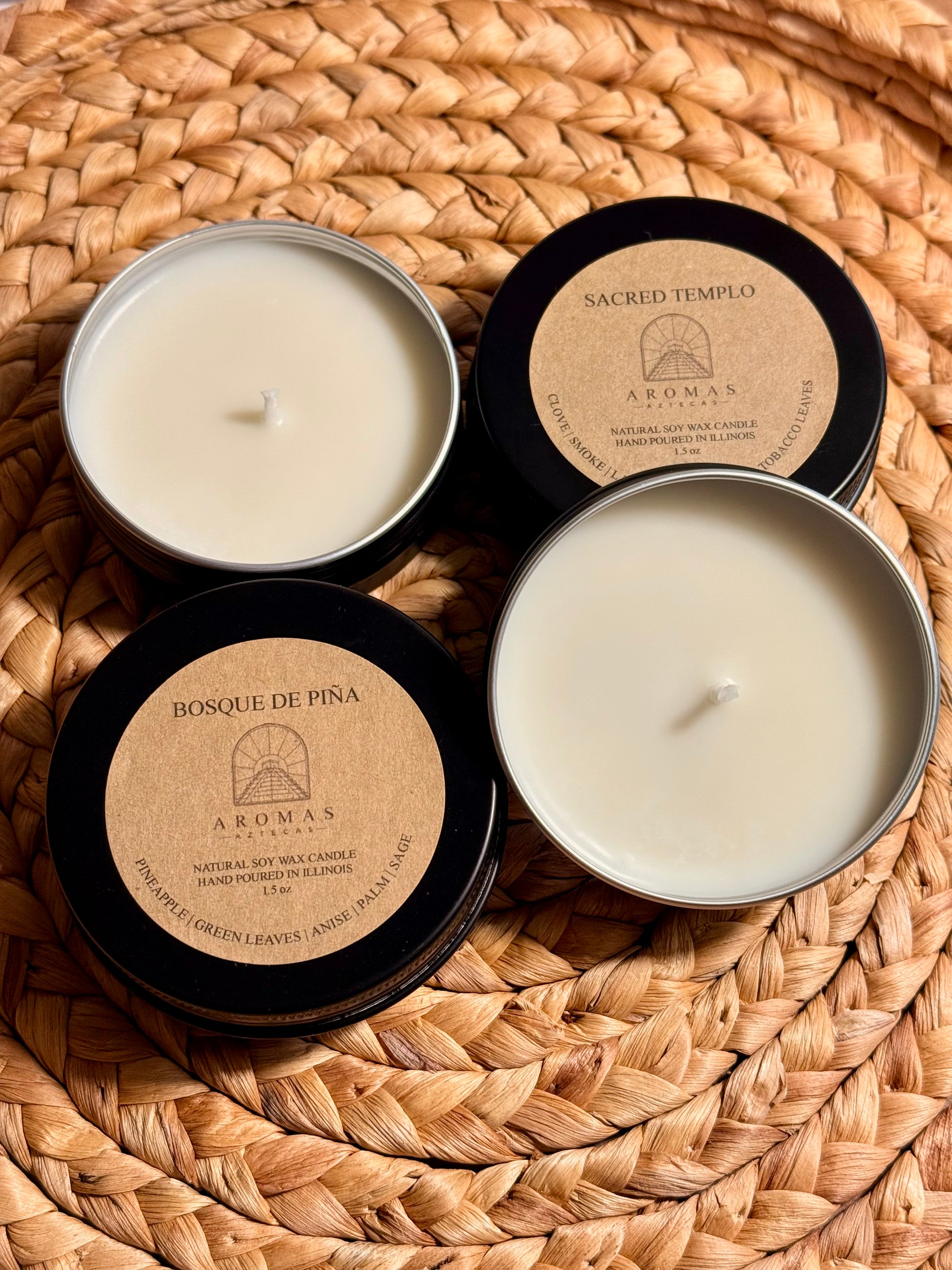 Aromas Aztecas discovery soy candle set featuring Sacred Templo and Bosque de Piña fragrance samples in black aluminum tins, displayed open on a woven textured surface with dried palm leaf décor.