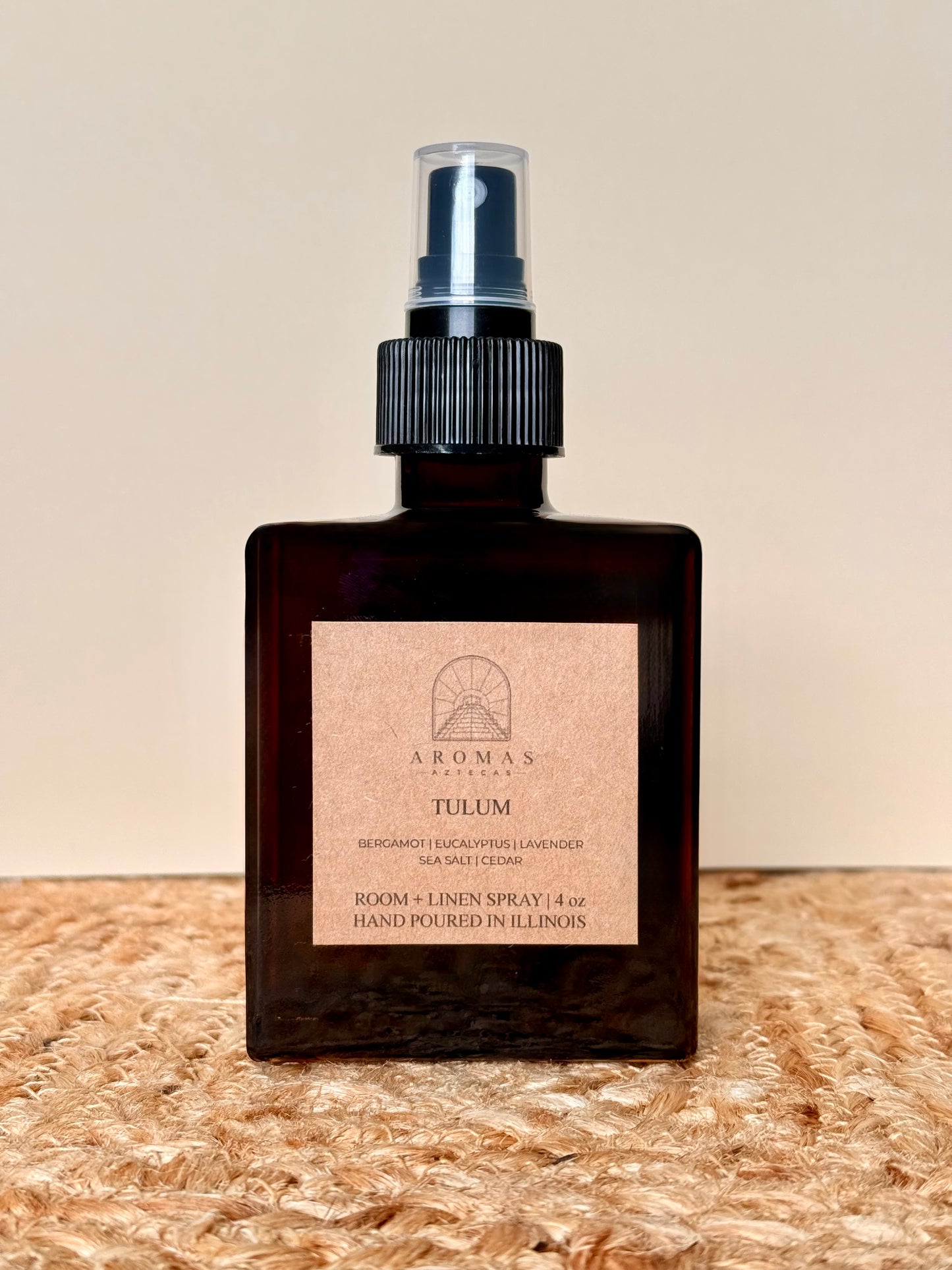 Aromas Aztecas Tulum room and linen spray in an amber glass bottle on a woven textured surface.