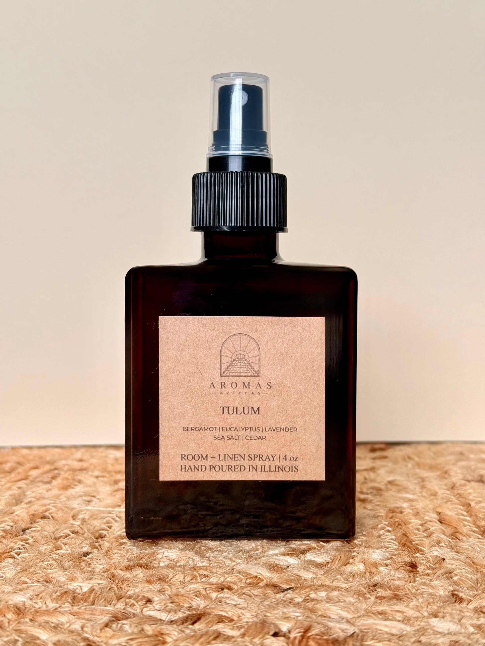 Aromas Aztecas Tulum room and linen spray in an amber glass bottle on a woven textured surface.
