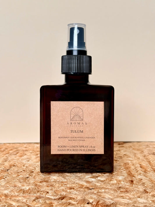 Aromas Aztecas Tulum room and linen spray in an amber glass bottle on a woven textured surface.