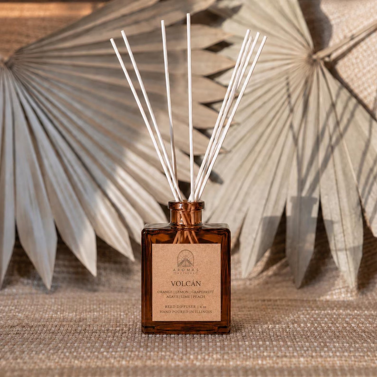 Aromas Aztecas Volcán reed diffuser in an amber glass bottle with natural reeds and dried palm leaf décor.