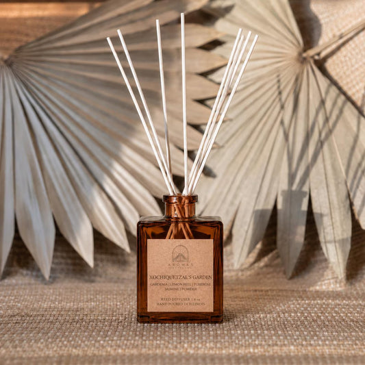 Aromas Aztecas Xochiquetzal's Garden reed diffuser in an amber glass bottle with natural reeds and dried palm leaf décor.